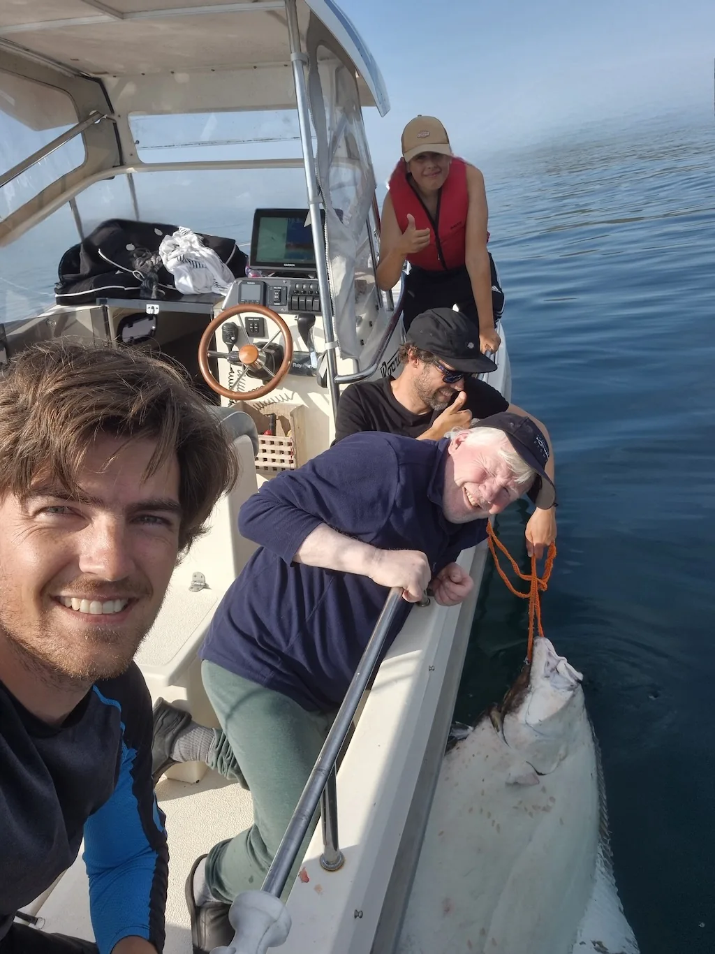 Anglers share a moment aboard a boat while a fish is held alongside in the water.
