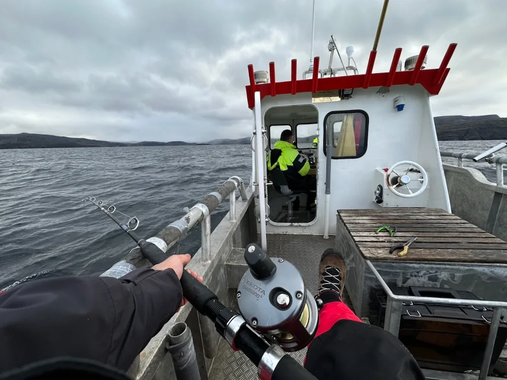 A fishing rod and reel in the foreground of a cabin boat at sea.