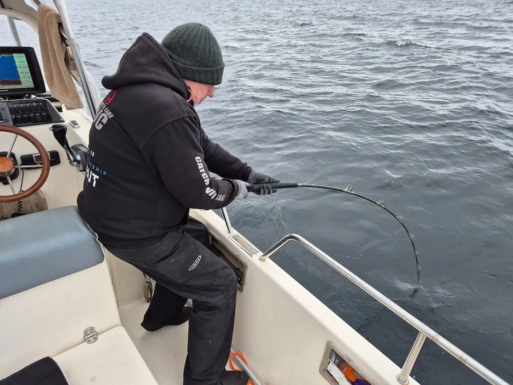 An angler works a bent fishing rod beside the rail of a boat.