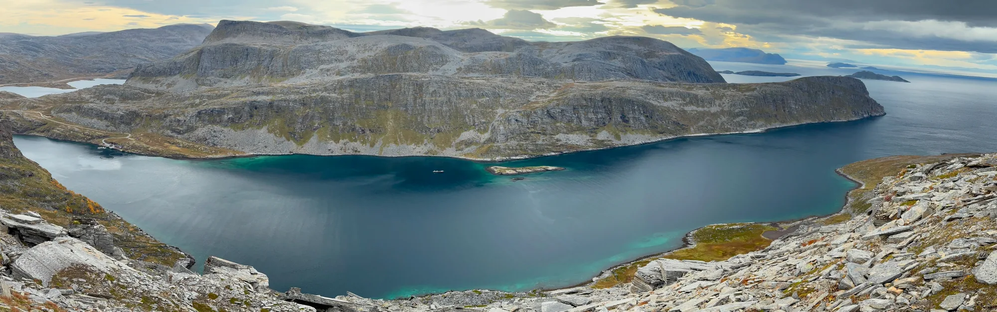 A panoramic view over blue fjord water, rocky headlands and the open coast.