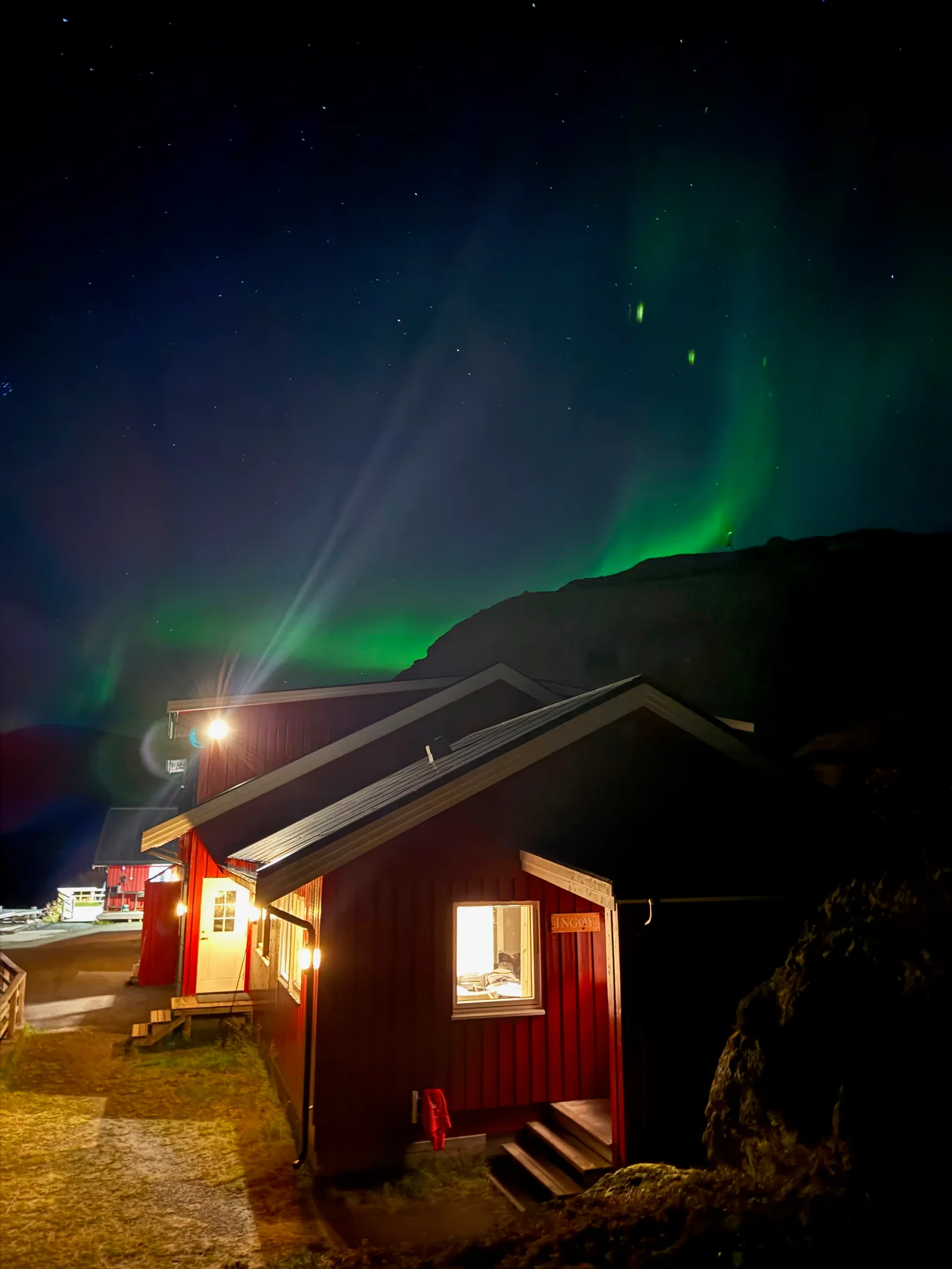 Green northern lights above red waterfront buildings at night.