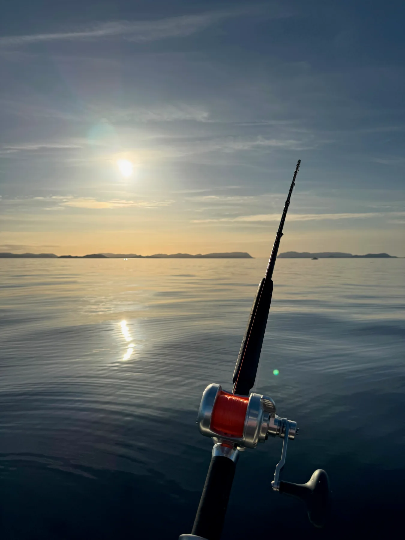 A fishing rod and reel above calm water reflecting the low sun.