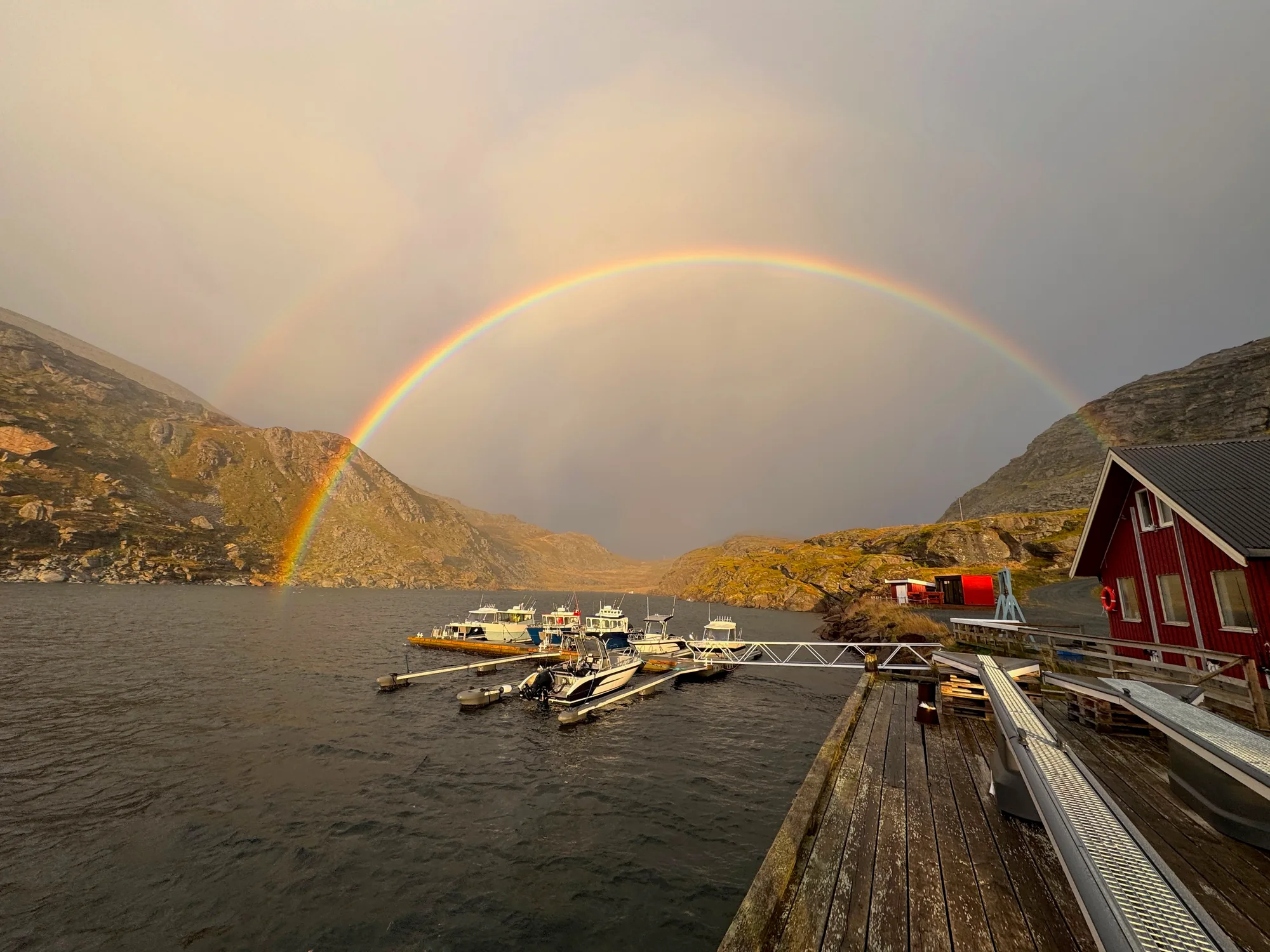 A rainbow arches above boats at the jetty and red waterfront buildings.