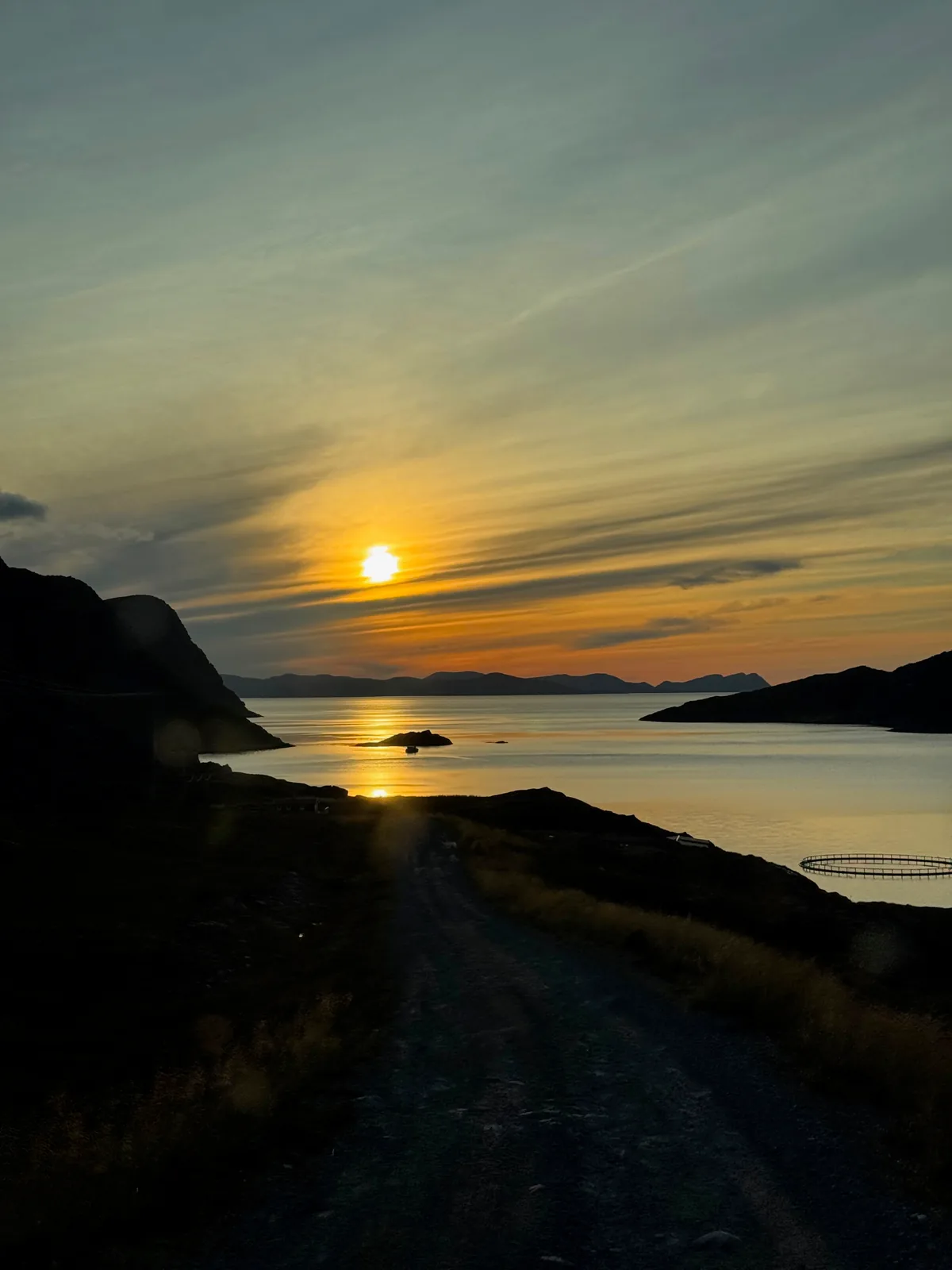A rocky coastal track under a low sun beside still water.