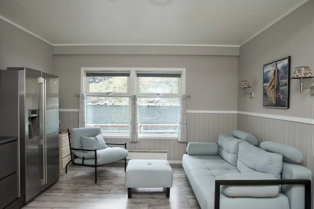 The Måsøy apartment lounge with seating beside a window overlooking the water.