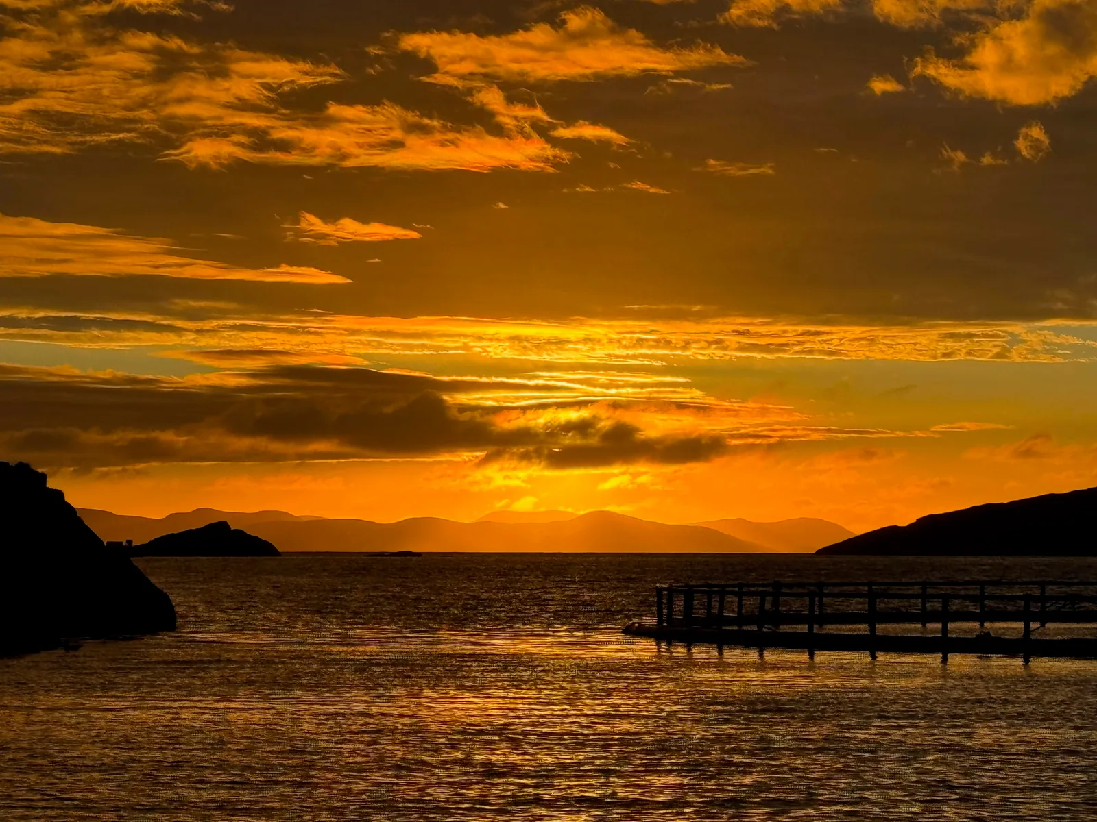 A vivid orange sunset over coastal water and low islands.