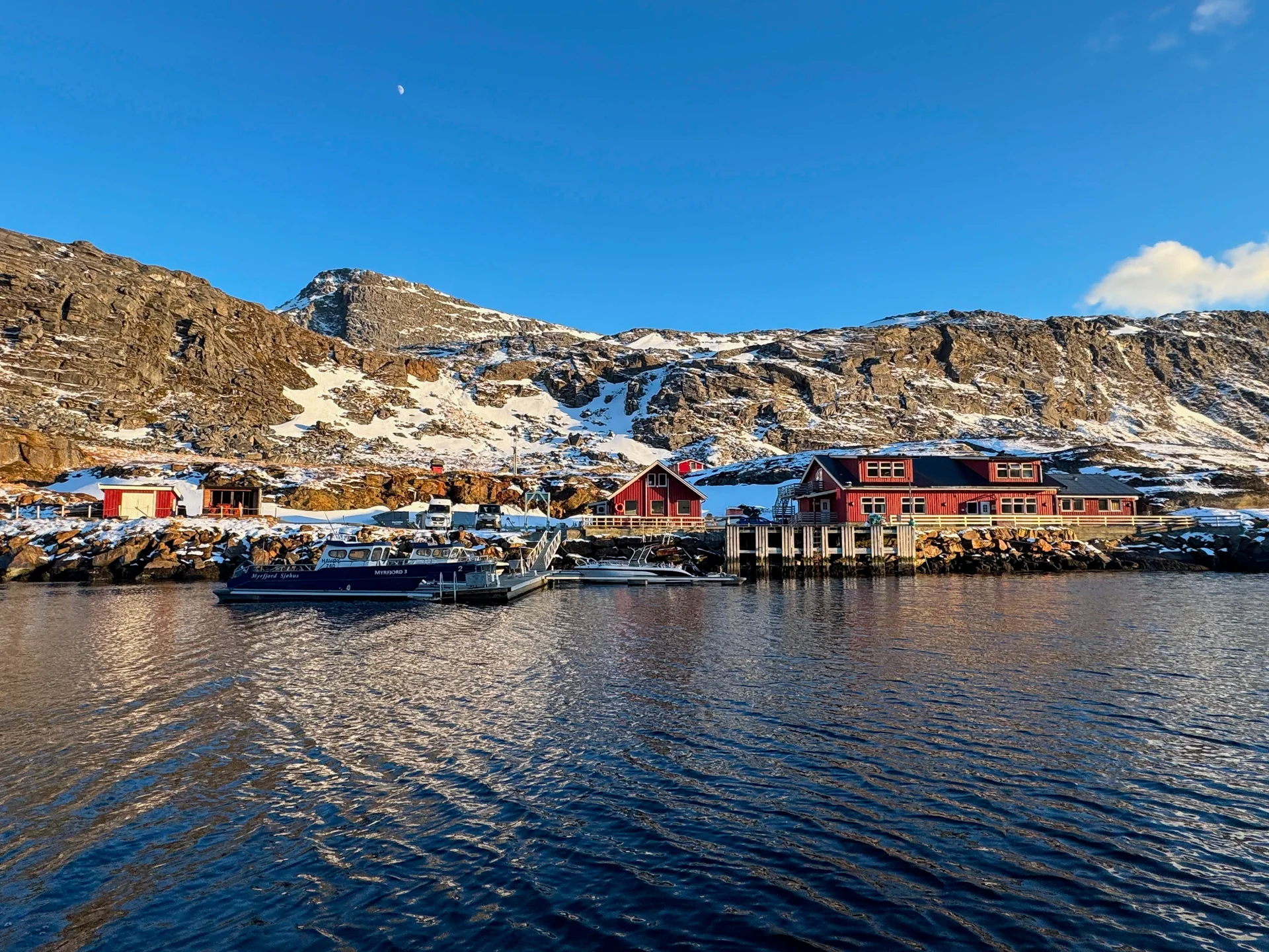 Red Myrfjord waterfront buildings and boats beside the fjord under a clear sky.