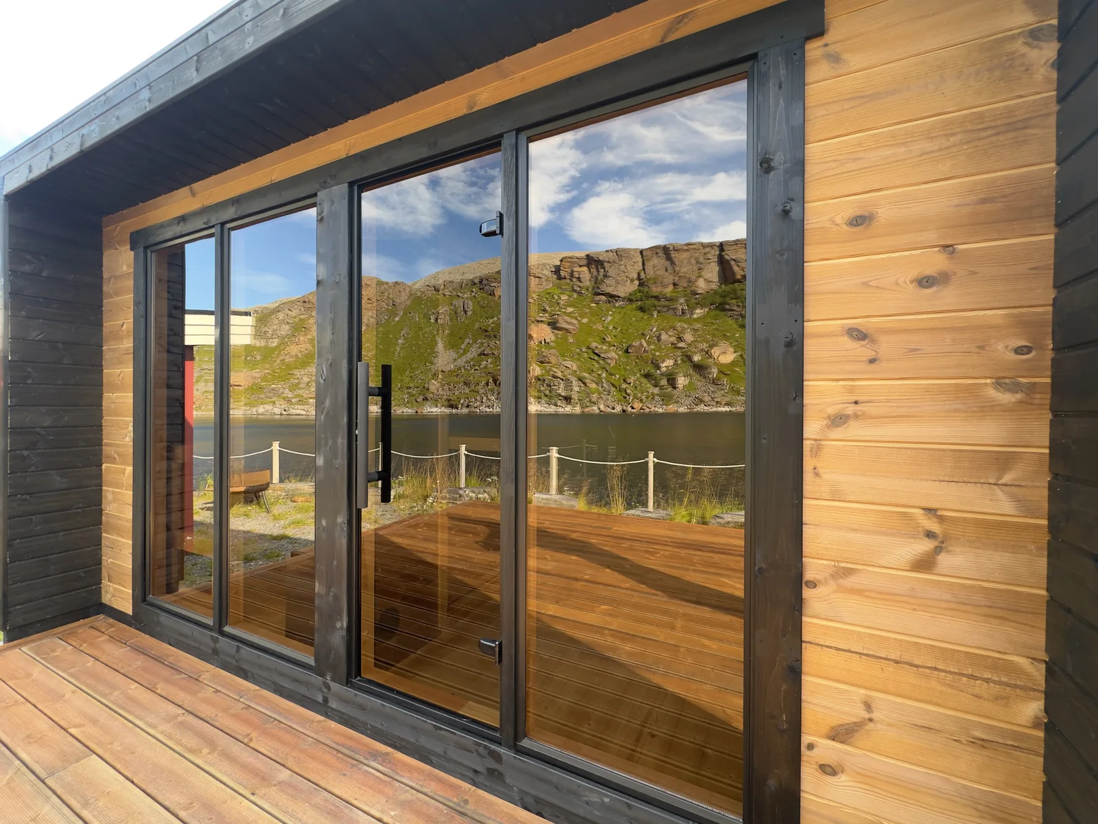 A glass-front sauna opens onto a wooden terrace by the coast.