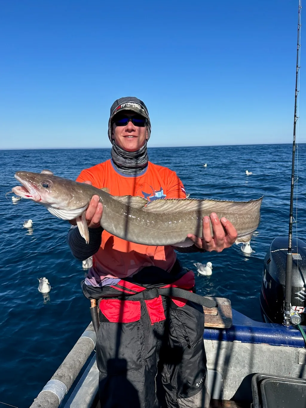 Angler holding a long sea fish aboard a boat on a sunny day