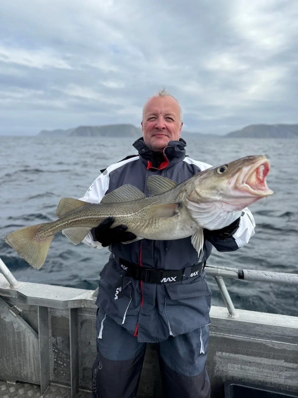 Angler holding a large sea fish with the northern coastline behind