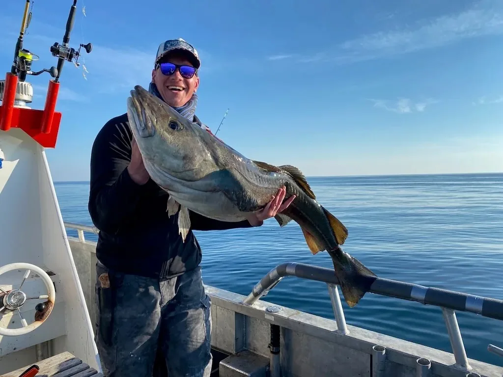 An angler holding a large fish aboard a boat at sea.